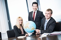 Drei HOFER Regionalverkaufsleiter sind in einem Büro und zeigen auf einen Globus auf dem Tisch.